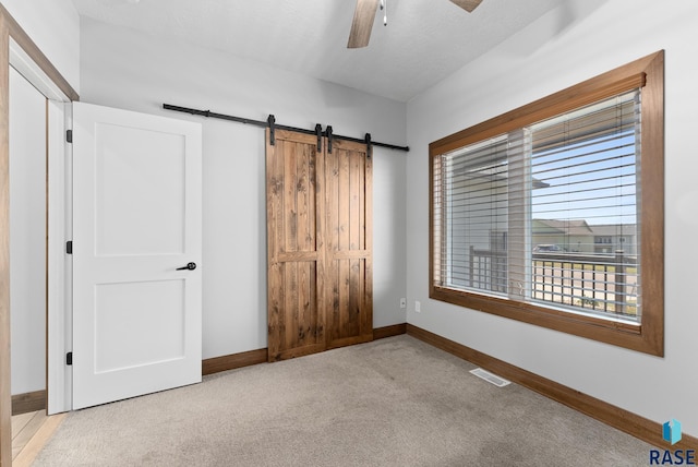 unfurnished bedroom featuring carpet flooring, baseboards, visible vents, and a barn door