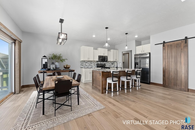 dining room with recessed lighting, baseboards, a barn door, and light wood-type flooring