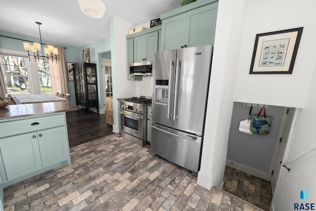 kitchen featuring green cabinetry, a notable chandelier, appliances with stainless steel finishes, brick floor, and baseboards