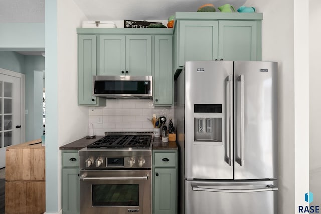 kitchen with dark countertops, appliances with stainless steel finishes, tasteful backsplash, and green cabinets