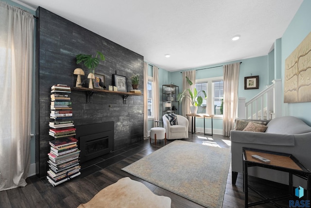 living room featuring dark wood-style flooring, an accent wall, stairway, recessed lighting, and a tiled fireplace