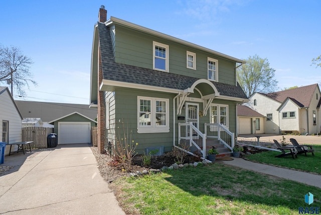 view of front of house with roof with shingles, a detached garage, a front yard, a chimney, and concrete driveway