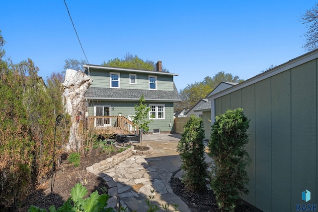 rear view of house with roof with shingles, a patio, a chimney, and a deck