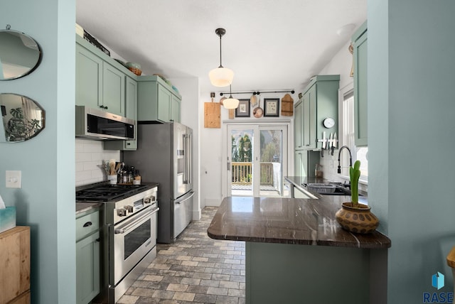 kitchen featuring green cabinetry, brick floor, tasteful backsplash, a sink, and stainless steel appliances