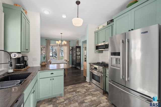 kitchen with an inviting chandelier, dark countertops, a sink, green cabinets, and stainless steel appliances