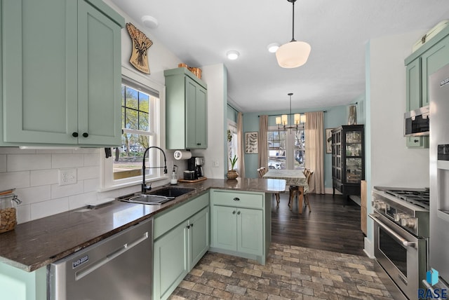 kitchen featuring a peninsula, dark countertops, a sink, appliances with stainless steel finishes, and green cabinets