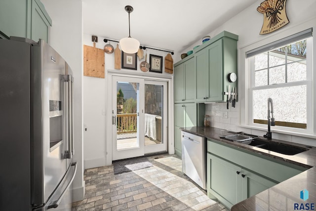 kitchen featuring appliances with stainless steel finishes, tasteful backsplash, a sink, green cabinets, and brick floor