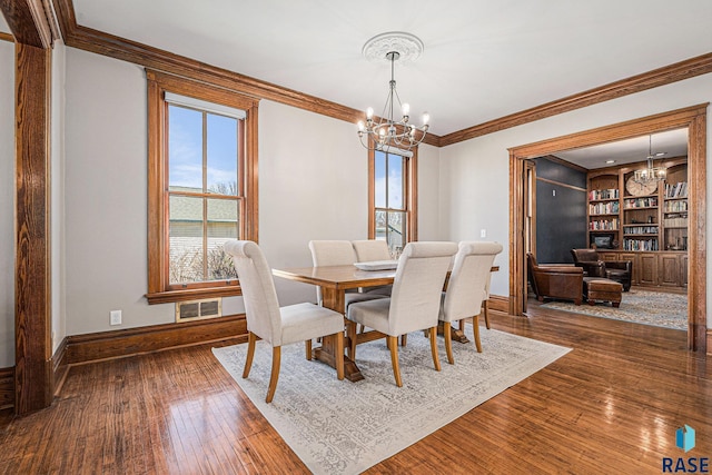 dining space with an inviting chandelier, baseboards, crown molding, and visible vents