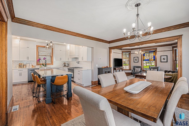 dining space with visible vents, ornamental molding, wood finished floors, and a notable chandelier