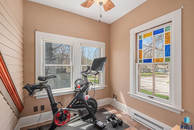 workout room featuring stone finish flooring, baseboards, a baseboard heating unit, and ceiling fan