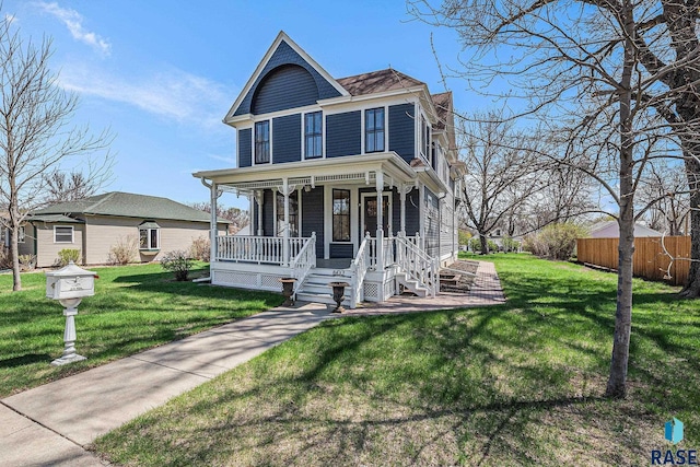 victorian home featuring covered porch, fence, and a front lawn