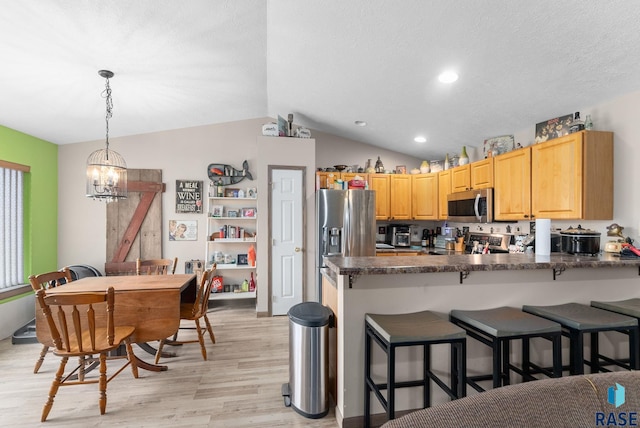kitchen with dark countertops, light wood-style floors, a chandelier, stainless steel appliances, and a peninsula