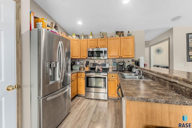 kitchen featuring dark countertops, appliances with stainless steel finishes, a sink, light wood-style floors, and a peninsula