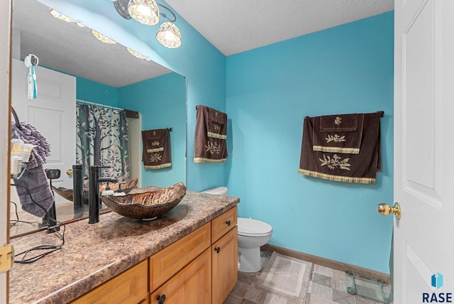 bathroom with a textured ceiling, curtained shower, vanity, baseboards, and toilet