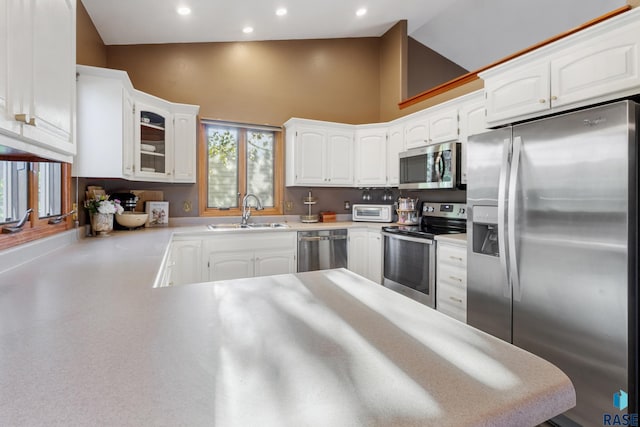 kitchen featuring appliances with stainless steel finishes, a sink, high vaulted ceiling, glass insert cabinets, and white cabinetry