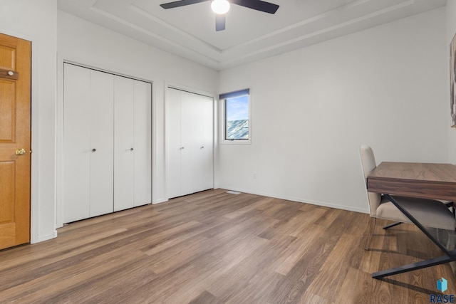 interior space featuring baseboards, a ceiling fan, a tray ceiling, and wood finished floors