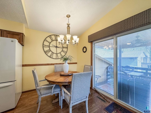 dining room with a textured ceiling, visible vents, vaulted ceiling, wood finished floors, and a chandelier