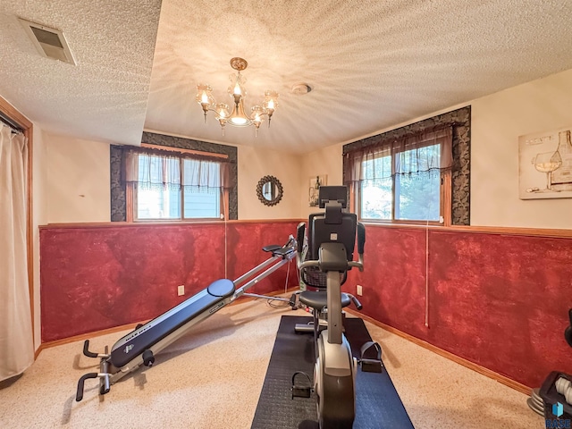 exercise room with a textured ceiling, visible vents, wainscoting, baseboards, and a notable chandelier