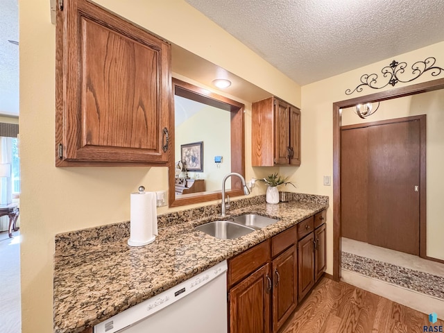 kitchen featuring light stone counters, a sink, dishwasher, a textured ceiling, and light wood-style flooring