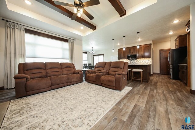 living area featuring beamed ceiling, recessed lighting, a raised ceiling, dark wood finished floors, and ceiling fan with notable chandelier
