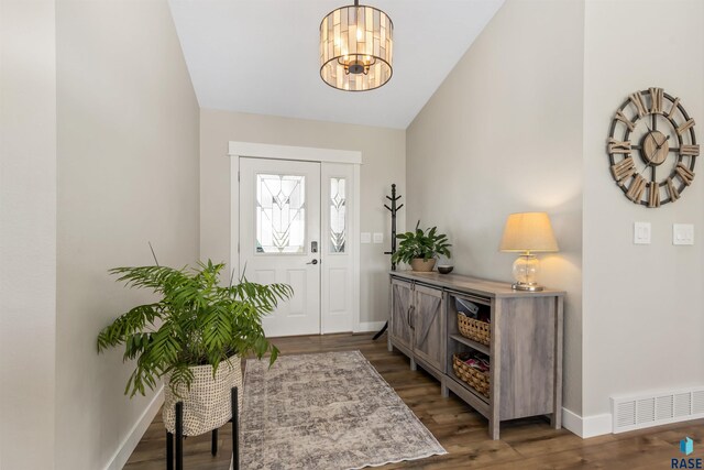 entrance foyer featuring a notable chandelier, baseboards, wood finished floors, lofted ceiling, and visible vents