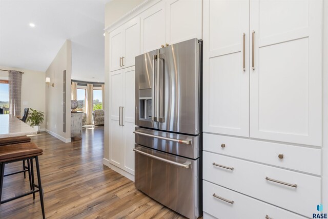 kitchen featuring baseboards, white cabinetry, stainless steel fridge with ice dispenser, light stone counters, and light wood-style flooring