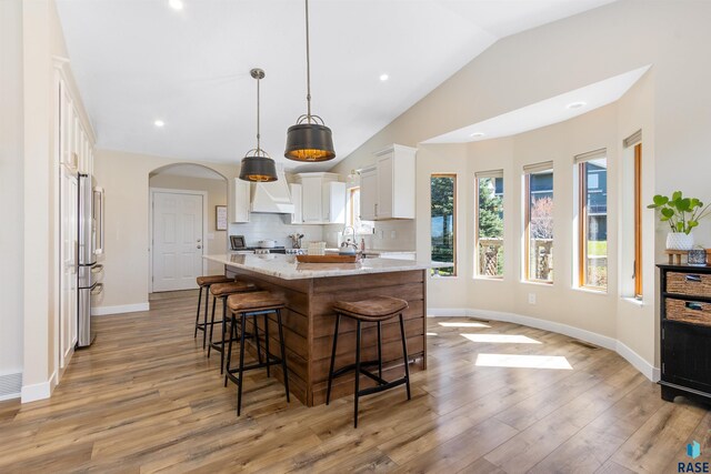 kitchen with a kitchen island with sink, a breakfast bar, light wood-type flooring, white cabinets, and vaulted ceiling