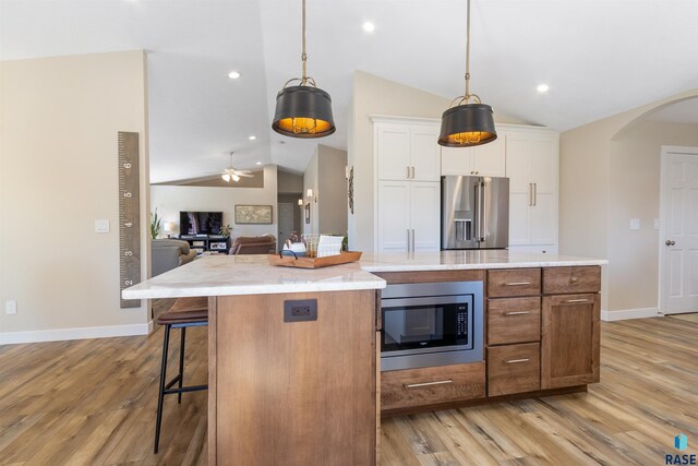 kitchen featuring appliances with stainless steel finishes, arched walkways, open floor plan, lofted ceiling, and light wood-style flooring