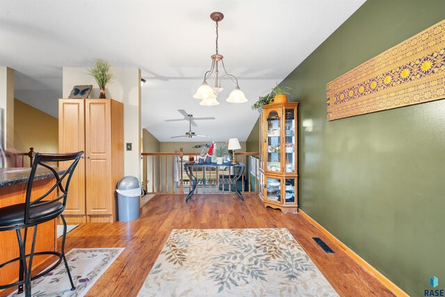dining space with ceiling fan with notable chandelier, baseboards, wood finished floors, lofted ceiling, and visible vents