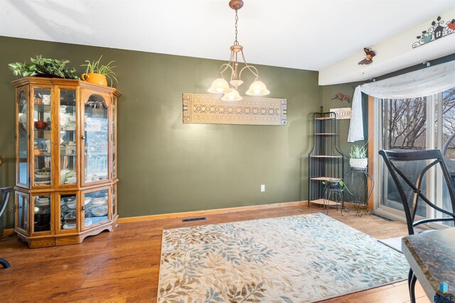 interior space featuring baseboards, a notable chandelier, visible vents, and wood finished floors