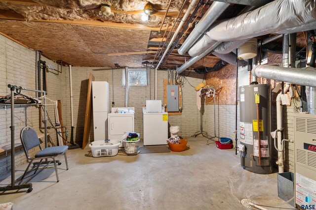 basement featuring washing machine and clothes dryer, brick wall, electric panel, and gas water heater