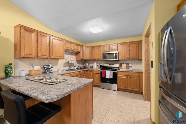 1012 E Magnolia Dr, Brandon, SD 57005 - kitchen with a peninsula, a breakfast bar area, tasteful backsplash, appliances with stainless steel finishes, and light tile patterned floors