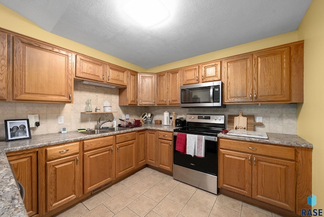 kitchen with a sink, appliances with stainless steel finishes, decorative backsplash, and light tile patterned flooring