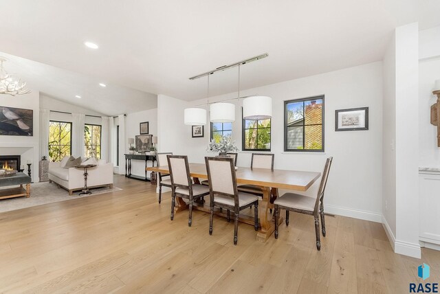 dining area with a glass covered fireplace, recessed lighting, baseboards, light wood-type flooring, and vaulted ceiling