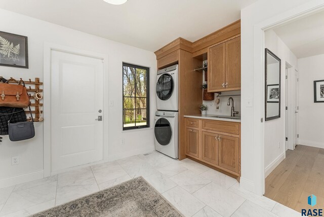 washroom with a sink, baseboards, stacked washer and dryer, and cabinet space