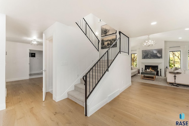 stairs with wood finished floors, baseboards, a notable chandelier, a glass covered fireplace, and recessed lighting