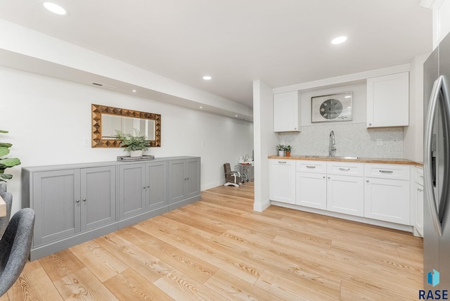 kitchen featuring tasteful backsplash, light wood-type flooring, a sink, white cabinets, and freestanding refrigerator