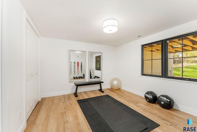 workout area with baseboards, light wood-type flooring, and visible vents