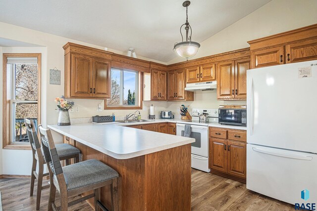 kitchen featuring a peninsula, lofted ceiling, white appliances, a kitchen breakfast bar, and under cabinet range hood