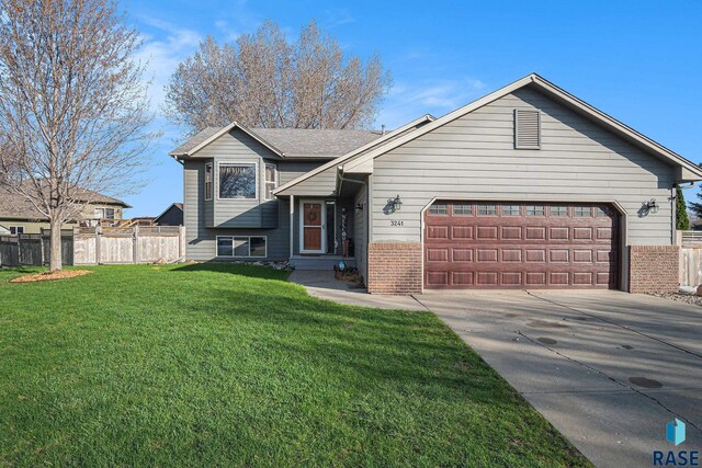 tri-level home with a garage, fence, a front yard, brick siding, and concrete driveway