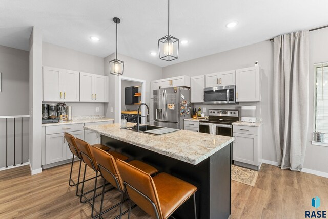 kitchen with a sink, stainless steel appliances, a kitchen bar, and light wood-style flooring