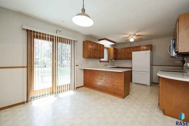 kitchen featuring a peninsula, ceiling fan, freestanding refrigerator, and brown cabinets