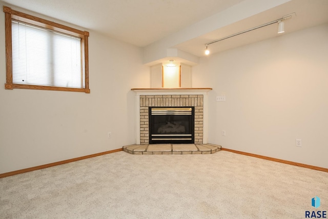 unfurnished living room with carpet floors, rail lighting, baseboards, and a brick fireplace