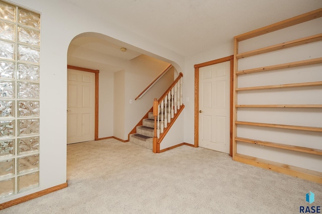 below grade area with arched walkways, baseboards, stairs, and carpet floors