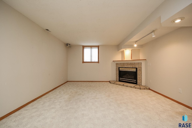 unfurnished living room with a brick fireplace, carpet flooring, track lighting, and baseboards