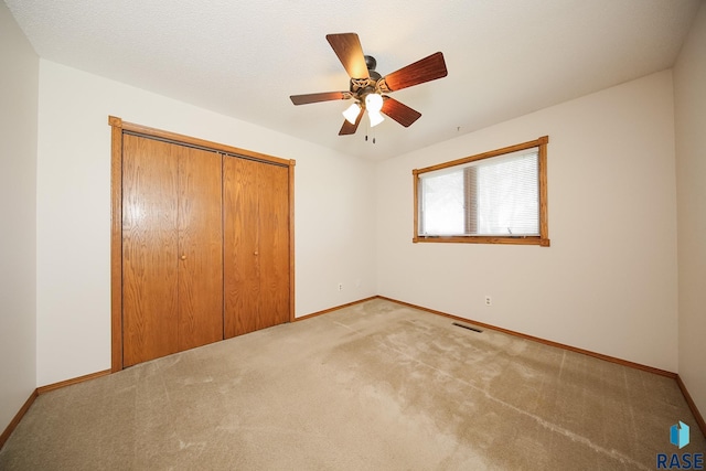 unfurnished bedroom featuring light colored carpet, a ceiling fan, baseboards, visible vents, and a closet