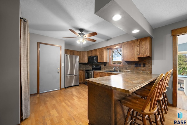 4108 E 23rd St, Sioux Falls, SD 57103 - kitchen featuring brown cabinetry, a peninsula, a kitchen bar, tasteful backsplash, and appliances with stainless steel finishes