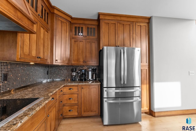kitchen with dark stone counters, freestanding refrigerator, and brown cabinets