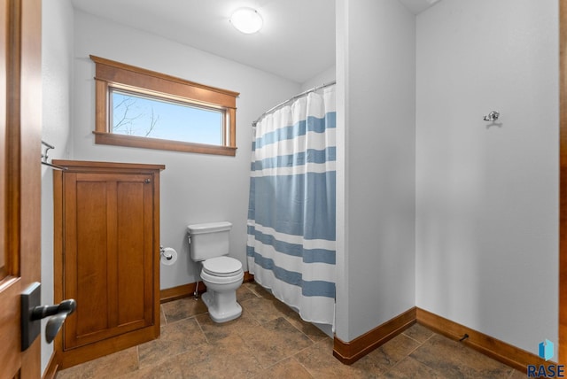 full bath with baseboards, a shower with shower curtain, stone tile flooring, and toilet