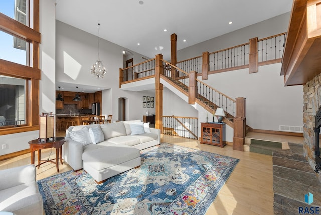 living area featuring visible vents, wood finished floors, a stone fireplace, a high ceiling, and a chandelier